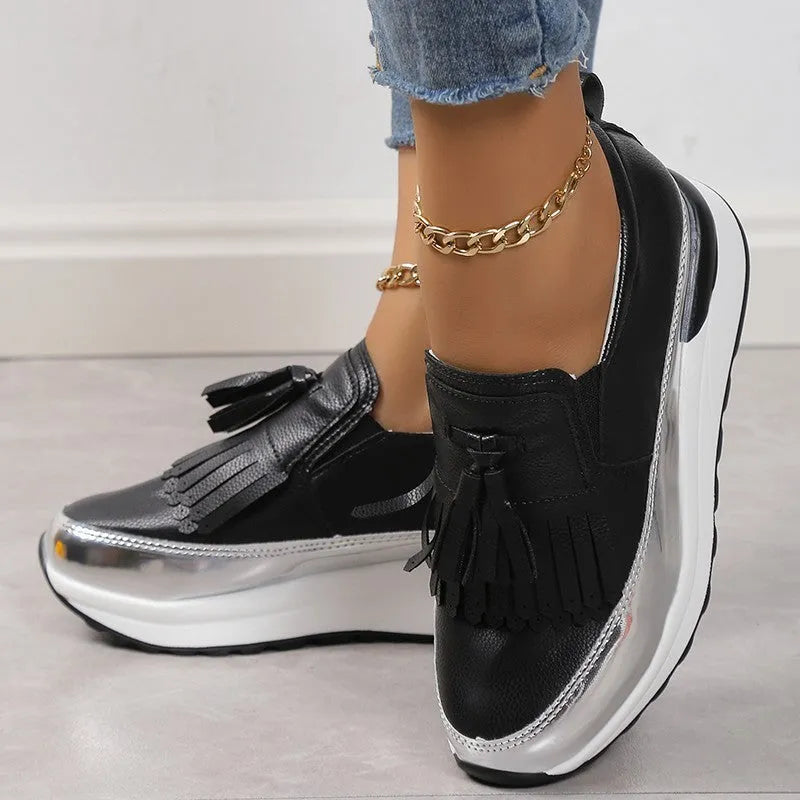 Women's black platform loafers with a tassel detail and a low wedge heel on a white background.