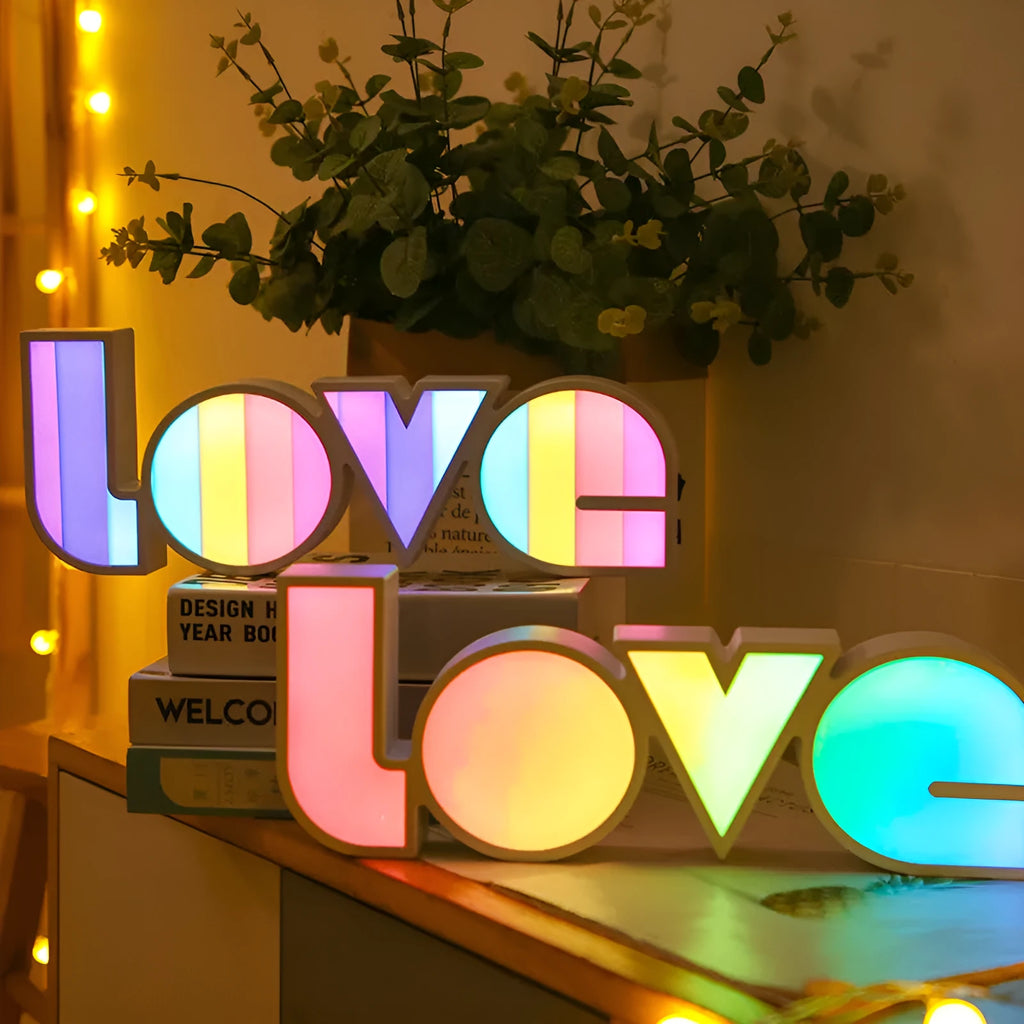 LED LOVE light with rainbow-coloured plastic shade on a desk.