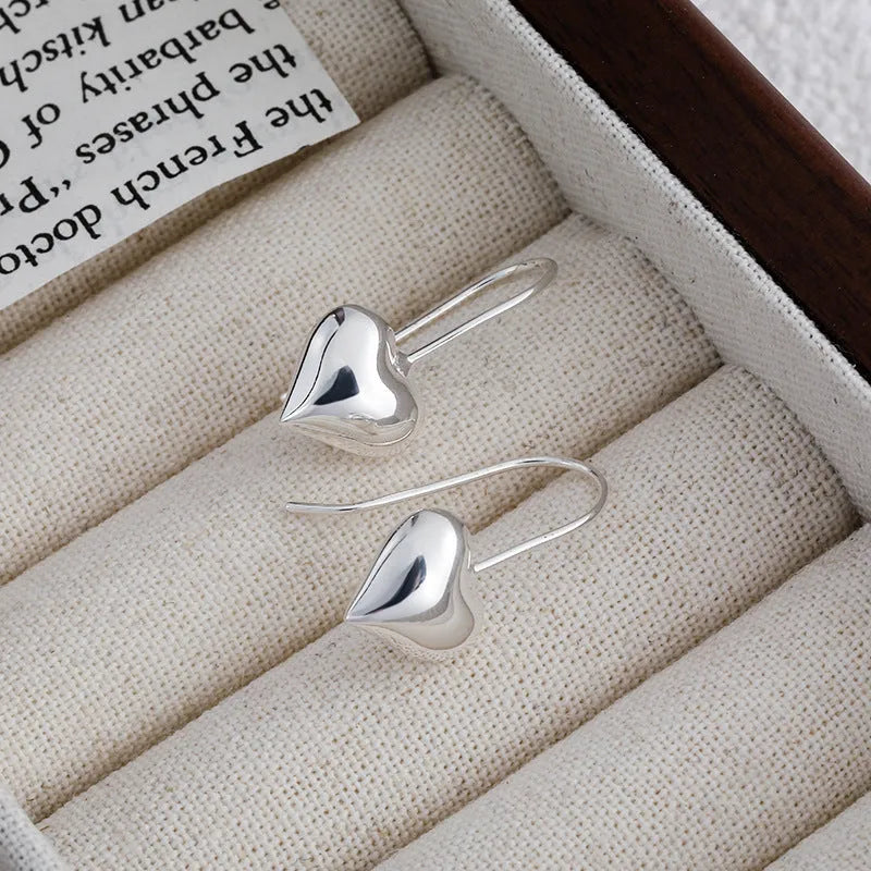Silver glossy 3D heart-shaped earrings with Korean style hooks on a white background.