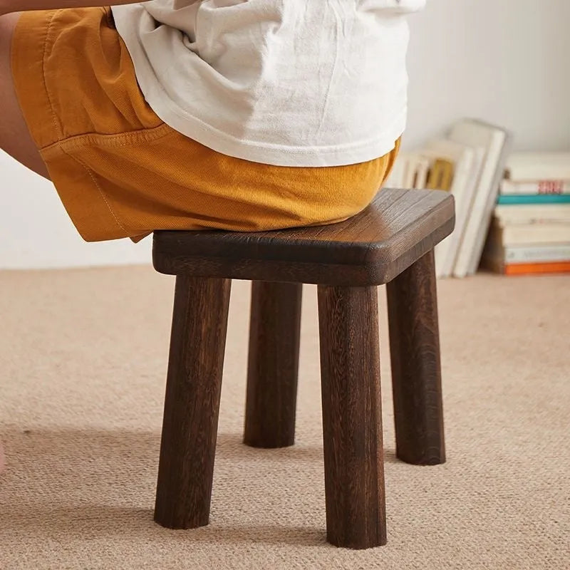 Distressed solid wood household stool for changing shoes in a living room setting.