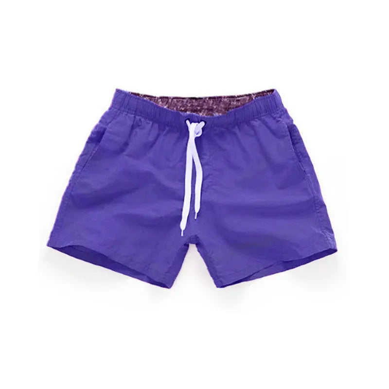 Men's straight-leg polyester surf shorts on a beach, showing colour options like black, fluorescent yellow, and navy blue.