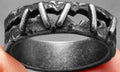 Close-up of a dark stainless steel double ring with punk-inspired stitching details on a finger.