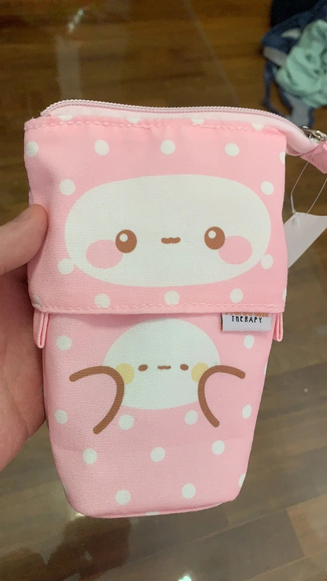 Pink polyester pencil case with zip closure on a desk, surrounded by pens and pencils
