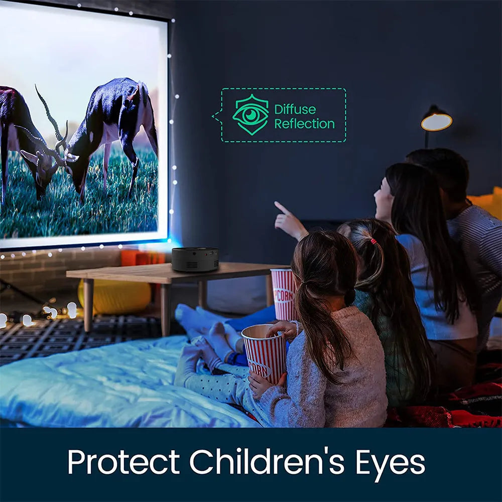 Black portable mini projector for children next to a mobile phone on a table.