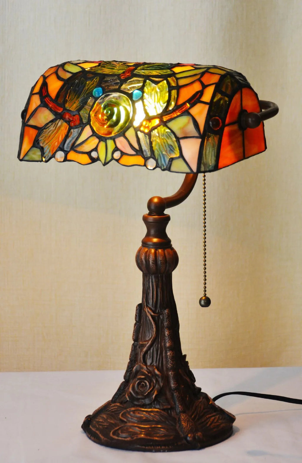 Tiffany style table lamp with coloured stained glass shade and resin base on a desk.