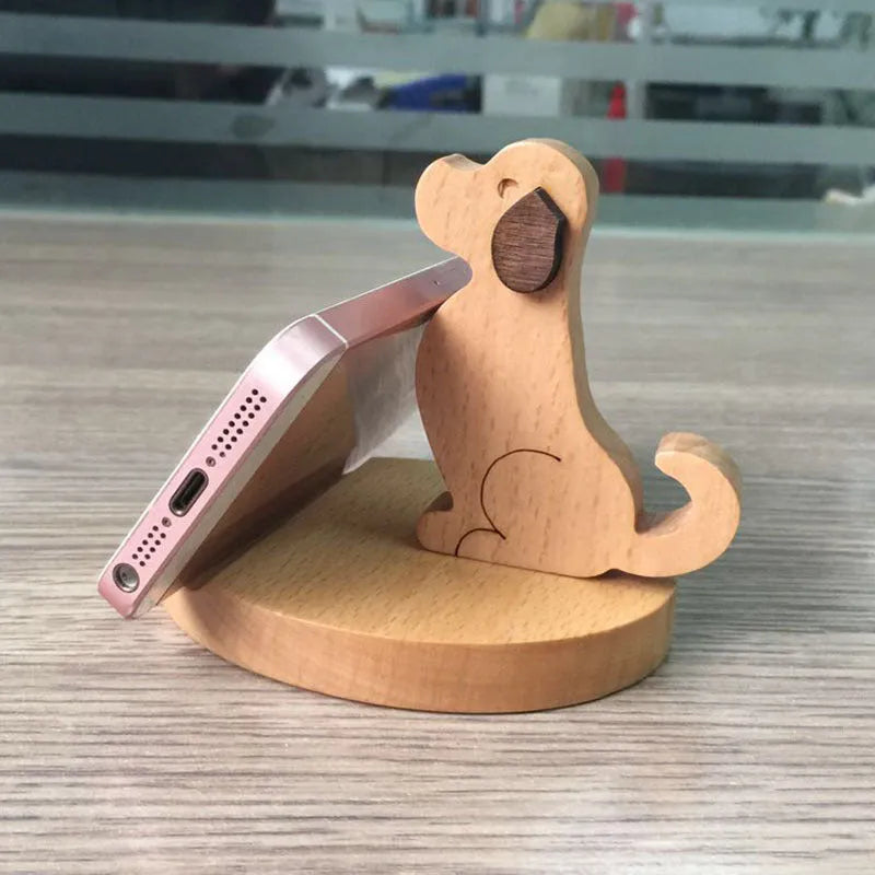 Solid beech wood mobile phone stand with a resin cow figurine and a slot for holding coins on a wooden desk.
