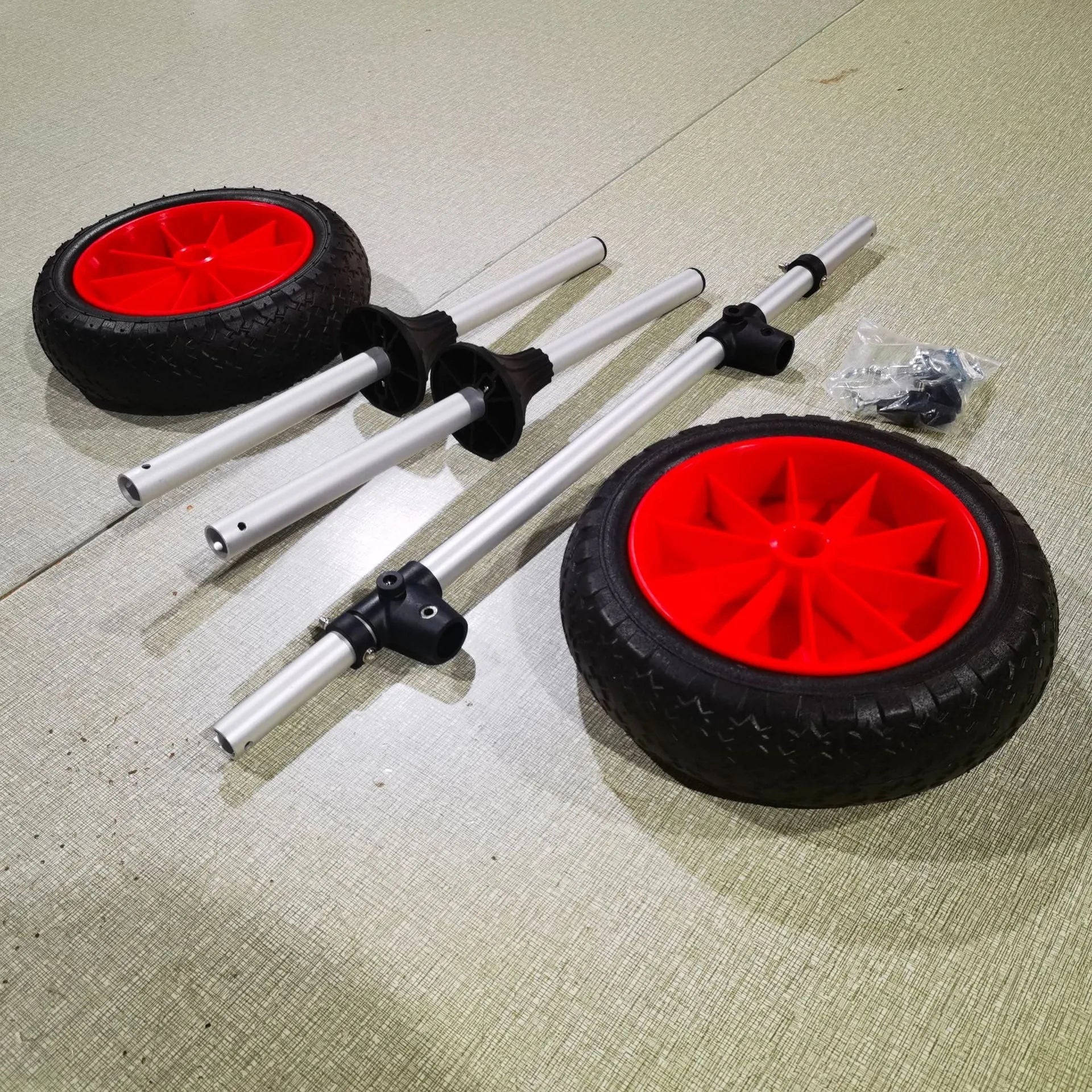 Foldable aluminium kayak beach trolley with solid rubber tyres, shown carrying a blue kayak on sand.