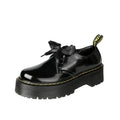 Women's black thick-soled leather shoes with ribbon and cross-strap details on a white background.