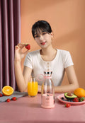 Pink and white handheld portable mini juicer with USB charging cable.