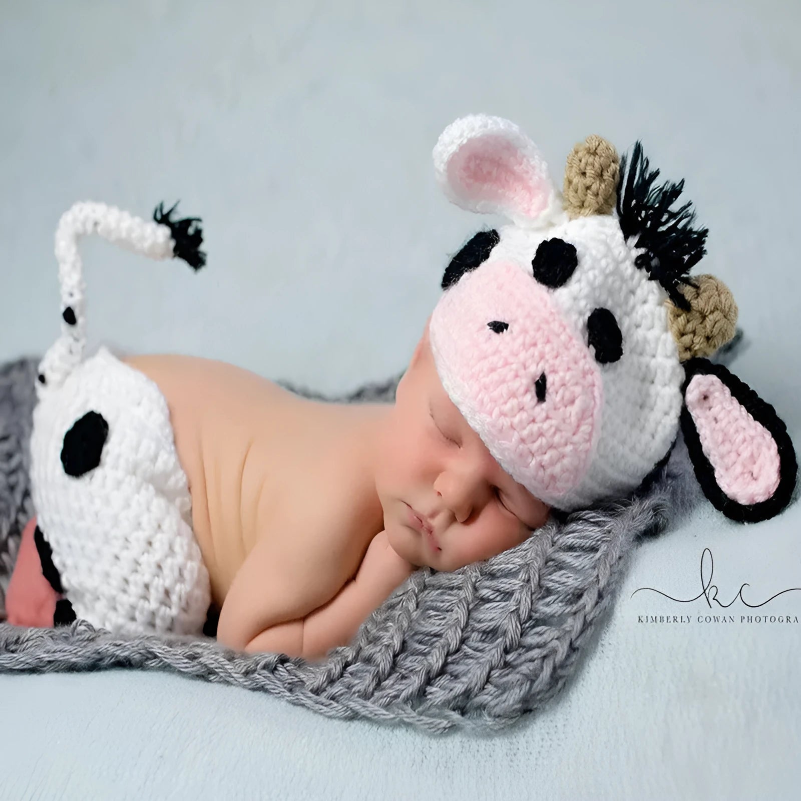 Hand-knitted white baby cow suit set with matching hat and pants on a newborn