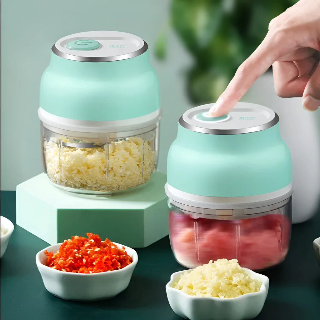 Portable white electric food chopper with transparent cup and stainless steel blades on a kitchen counter.