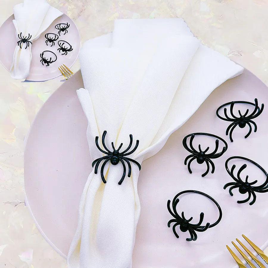 Six black alloy spider-shaped napkin rings for Halloween table decoration on a dark tablecloth.